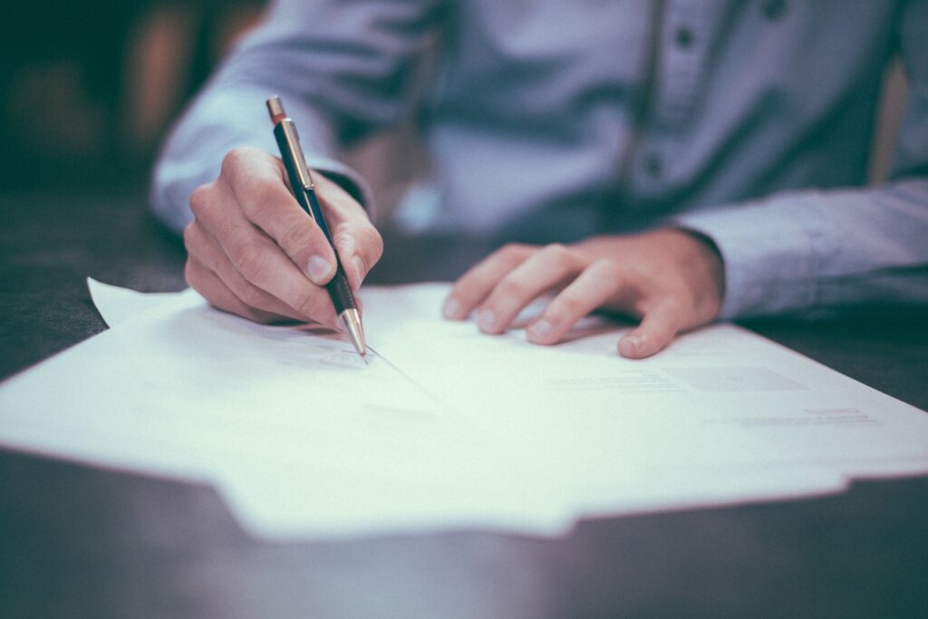 Person signing document with pen at desk