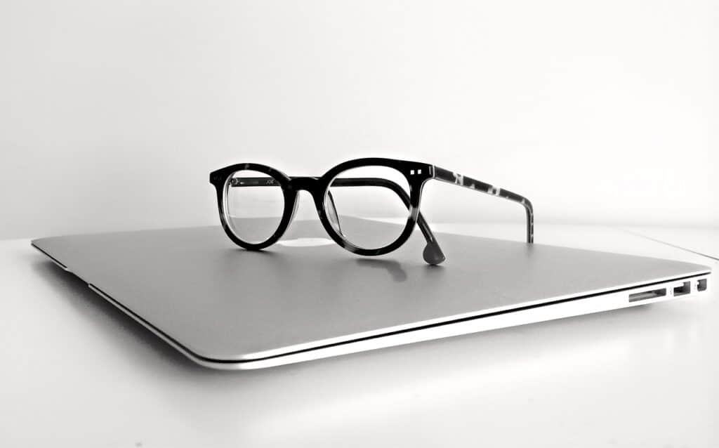 Black eyeglasses resting on closed silver laptop