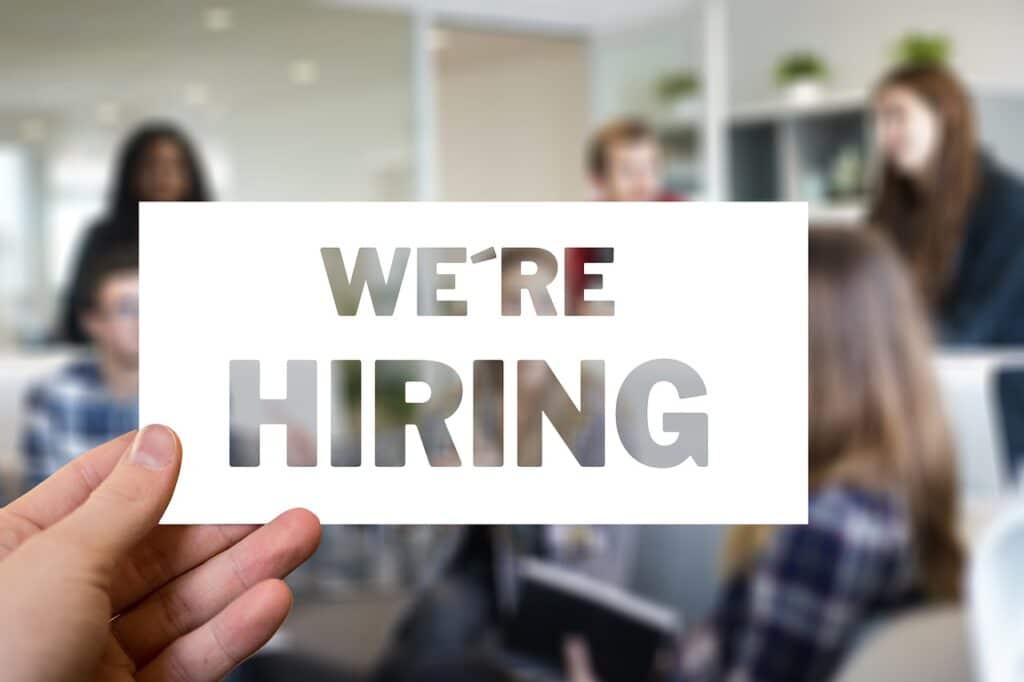 Hand holding "We're Hiring" sign in office