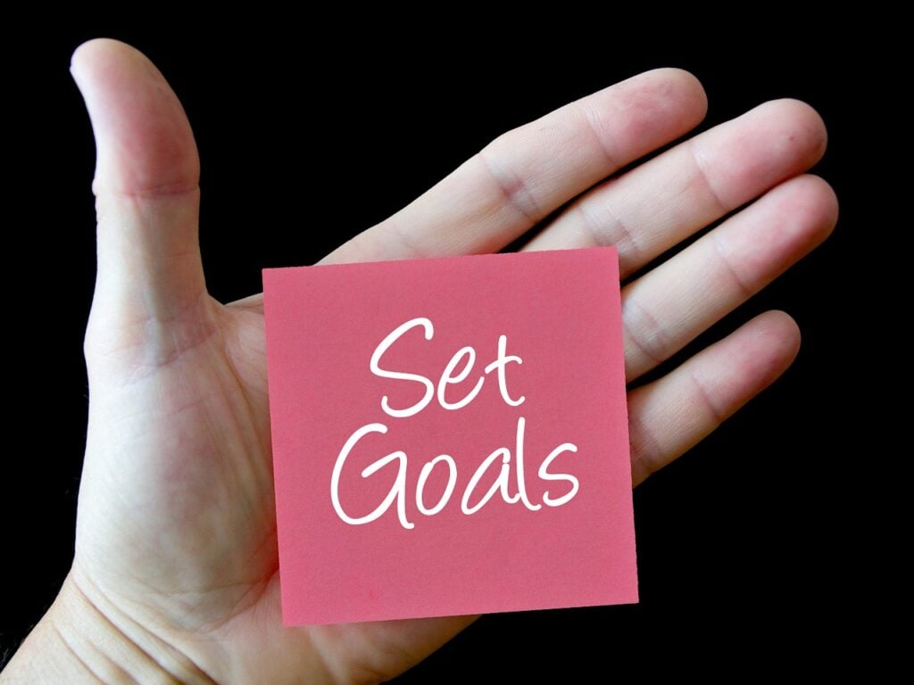 Hand holding pink card reading 'Set Goals'