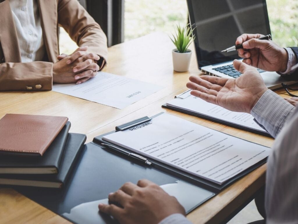 A close-up of a job interview taking place across a wooden desk