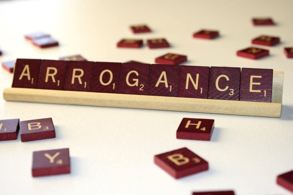 Scrabble tiles spelling arrogance on wooden rack