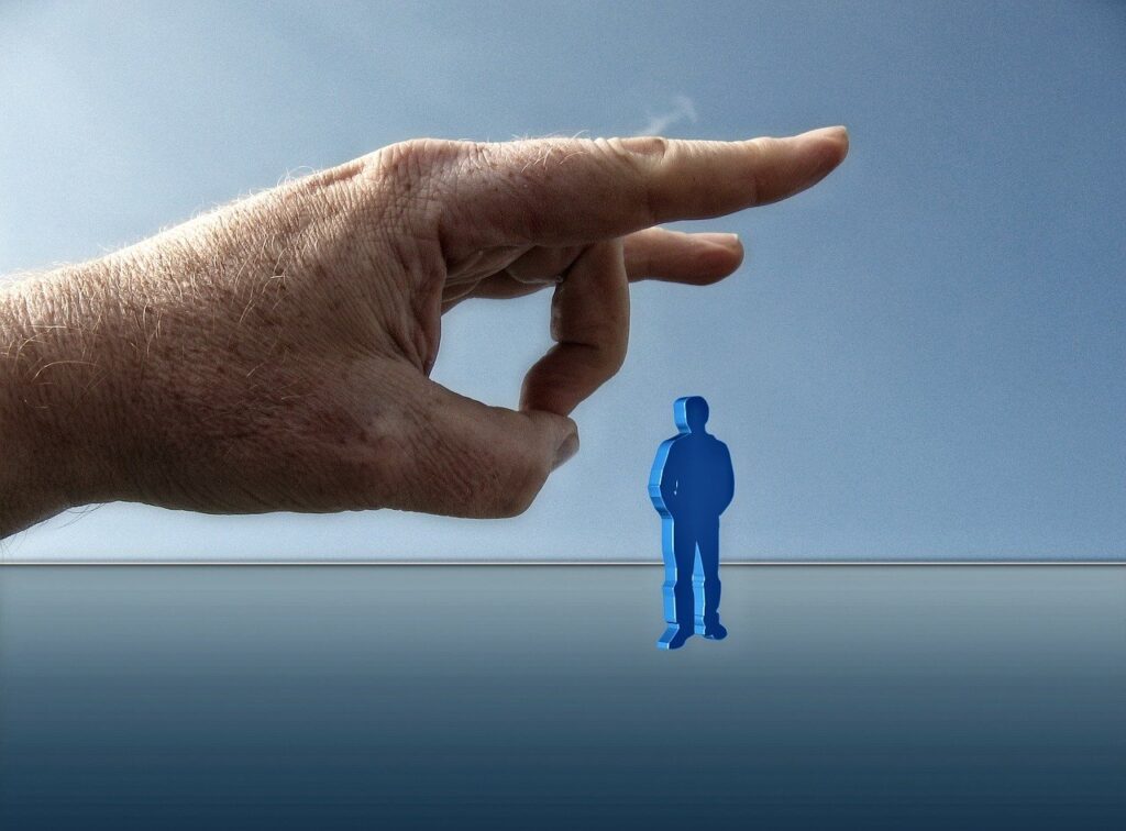 A large human hand hovering over a small, blue 3D figure of a person standing on a reflective surface.