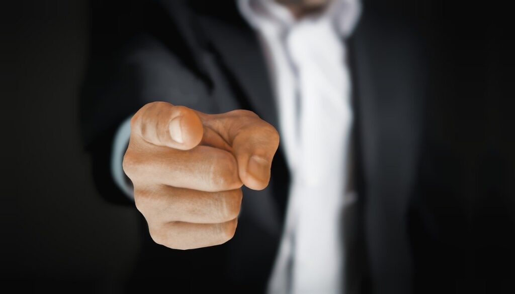 A person in a suit pointing their index finger directly at the camera.