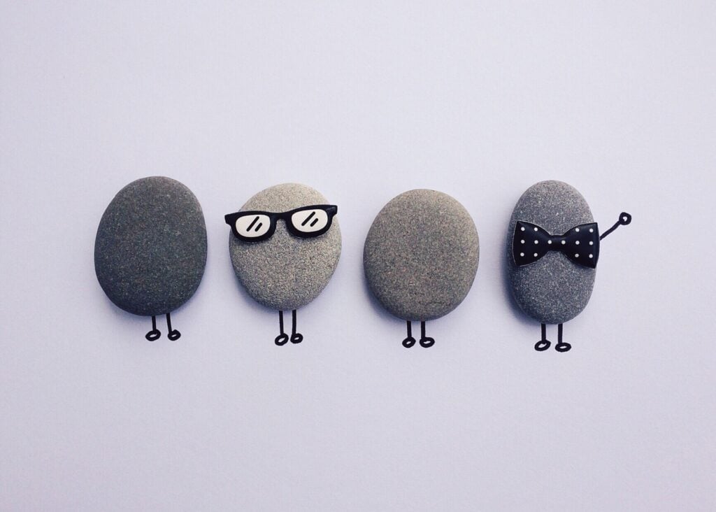 Four pebbles with drawn legs, one wearing glasses and another with a bow tie
