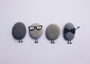 Four pebbles with drawn legs, one wearing glasses and another with a bow tie