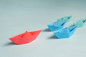 Red origami boat leading blue and green boats