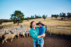 Smiling farmer holding a child near a flock of sheep in a rural area