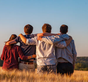 Four people standing in a field with their arms around each other