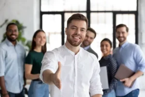 Smiling professional offering handshake with team in background