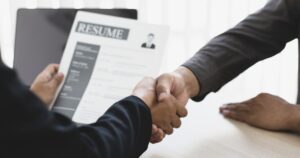 A hand holding a resume and shaking hands
