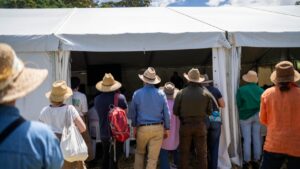 A group of people wearing wide-brimmed hats and casual outdoor clothing standing behind a white marquee tent