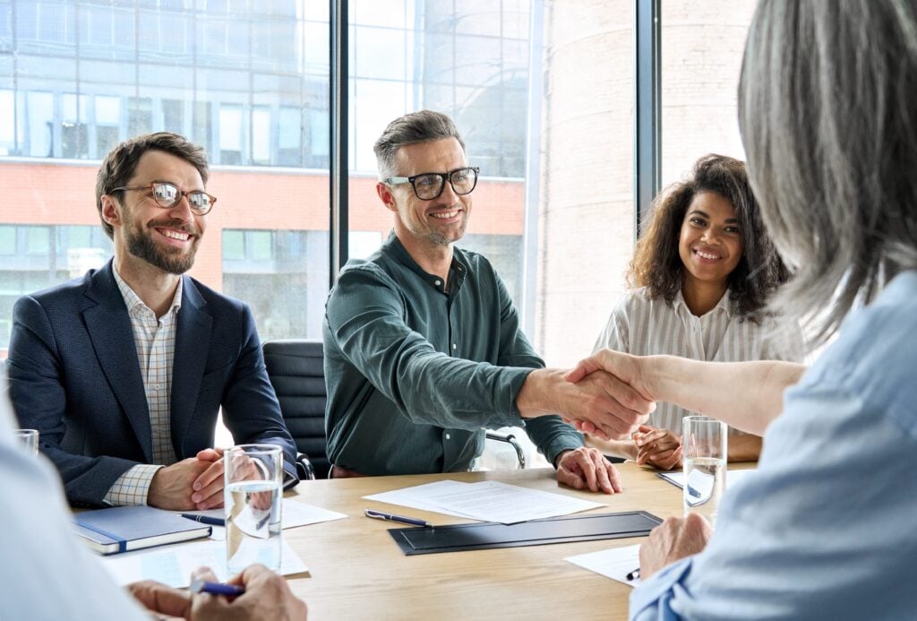A group of four business professionals is seated around a conference table.