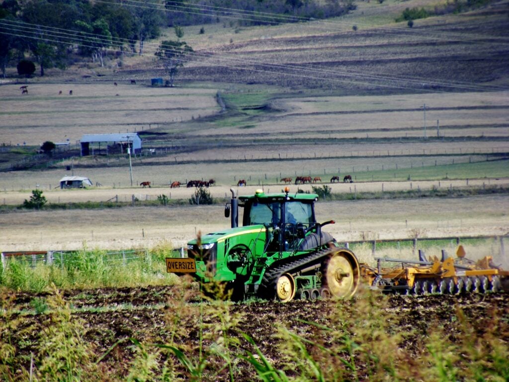 A green John Deere tracked tractor pulling a large yellow disc harrow through a field
