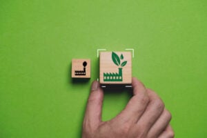 A hand placing a larger wooden block with a green "eco-friendly" factory icon