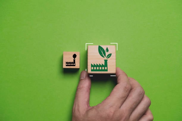 A hand placing a larger wooden block with a green "eco-friendly" factory icon