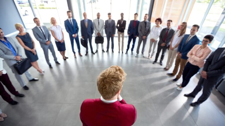 A person in a red suit standing before a large group of diverse business professionals