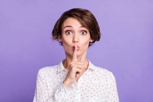 Photo of charming young lady finger covering mouth lips do not tell isolated on violet color background