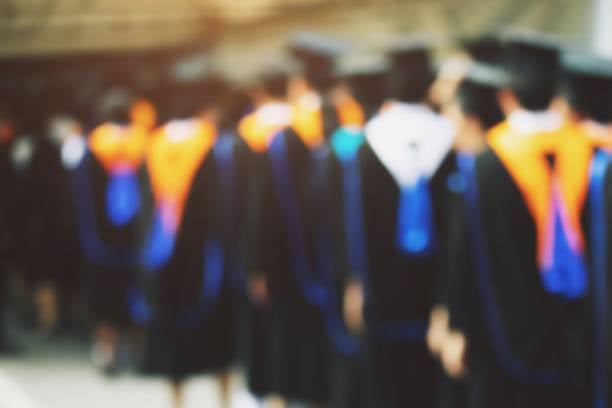 A blurred, back-view shot of a crowd of graduates in black academic gowns and mortarboards.