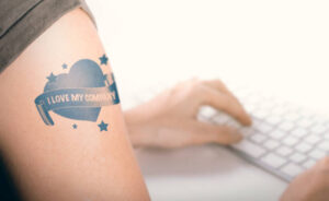 Woman working on a computer with close up on a tatoo with the text i love my company.