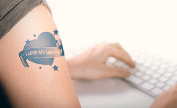 Woman working on a computer with close up on a tatoo with the text i love my company.