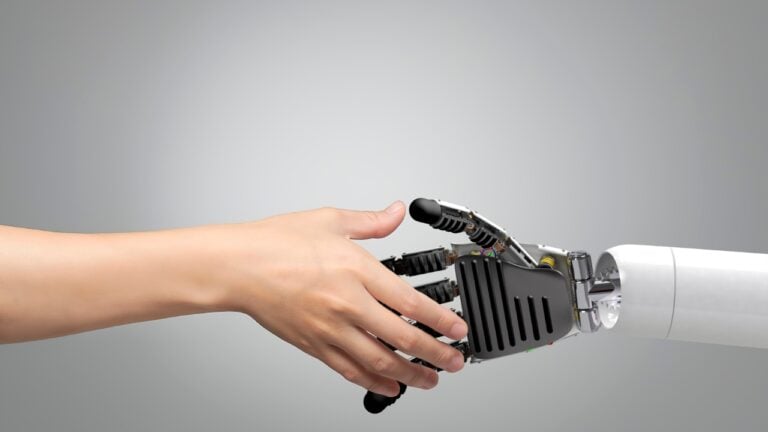 A human hand extending from the left to shake hands with a sleek robotic hand extending from the right.