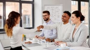 A panel of three smiling interviewers shaking hands with a female job candidate across a conference table.